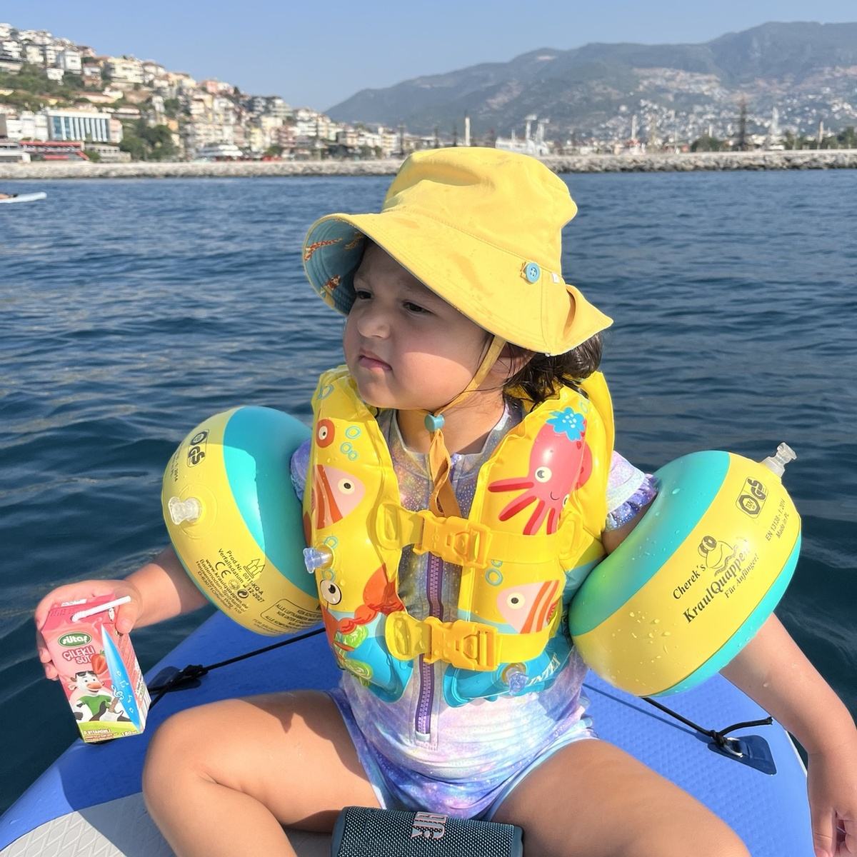 Young child in a life jacket and sun hat on a board