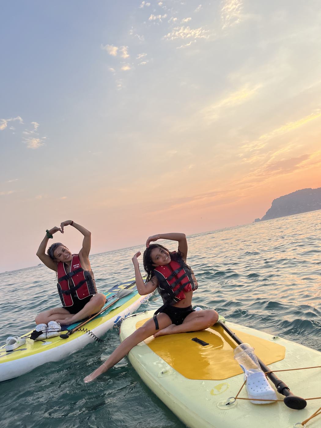Two friends on paddle boards under a pink dawn sky